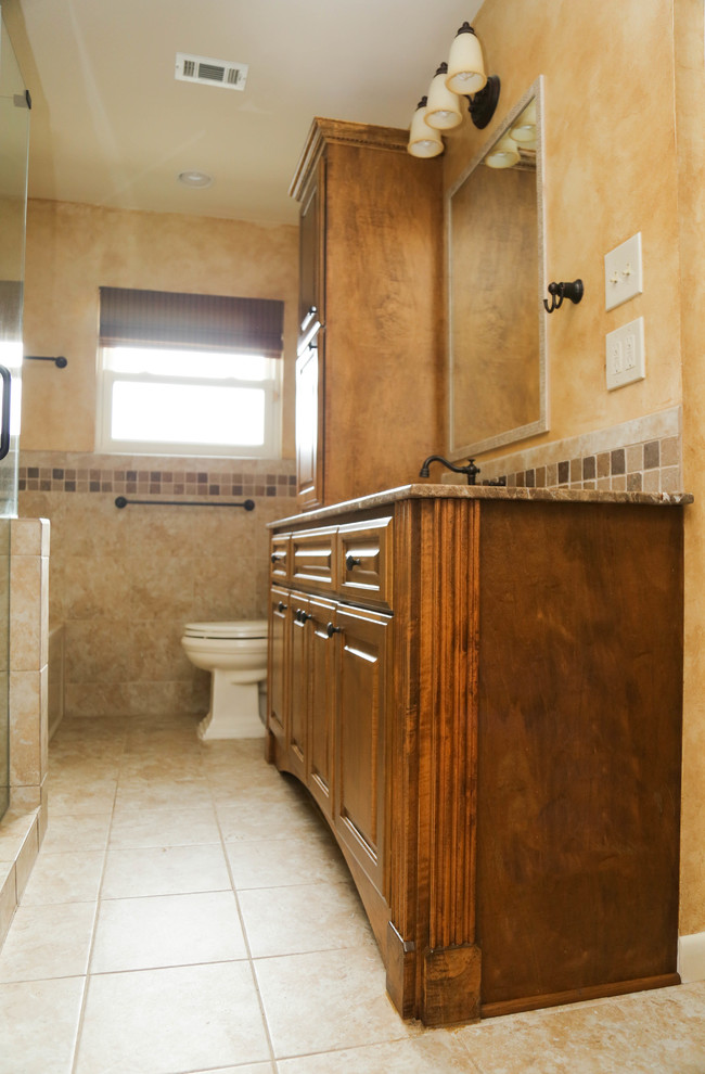 Пример оригинального дизайна: ванная комната среднего размера в классическом стиле с фасадами с выступающей филенкой, фасадами цвета дерева среднего тона, угловым душем, бежевой плиткой, каменной плиткой, бежевыми стенами, полом из керамической плитки, раздельным унитазом, бежевым полом, душевой кабиной, врезной раковиной, столешницей из гранита, душем с распашными дверями и ванной в нише