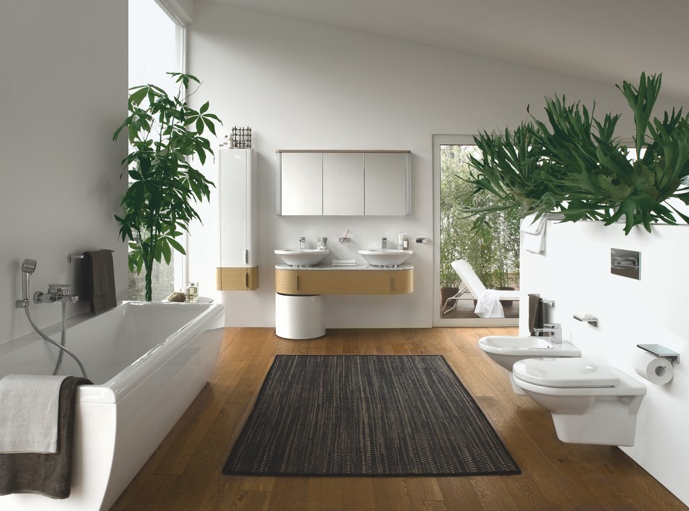 Идея дизайна: большая главная ванная комната в современном стиле с плоскими фасадами, светлыми деревянными фасадами, накладной ванной, душем над ванной, инсталляцией, белой плиткой, белыми стенами, настольной раковиной, мраморной столешницей и полом из бамбука