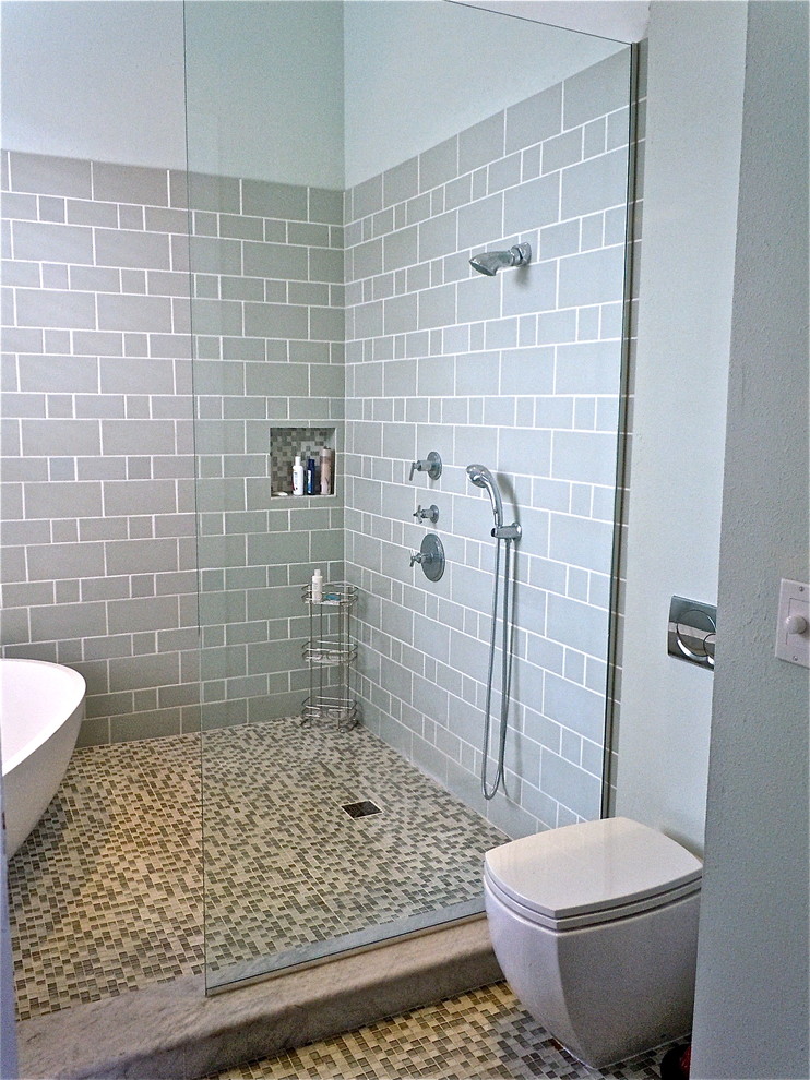 Photo of a modern ensuite bathroom in New Orleans with a vessel sink, flat-panel cabinets, dark wood cabinets, wooden worktops, a freestanding bath, a walk-in shower, a one-piece toilet, grey tiles, glass tiles, grey walls and mosaic tile flooring.