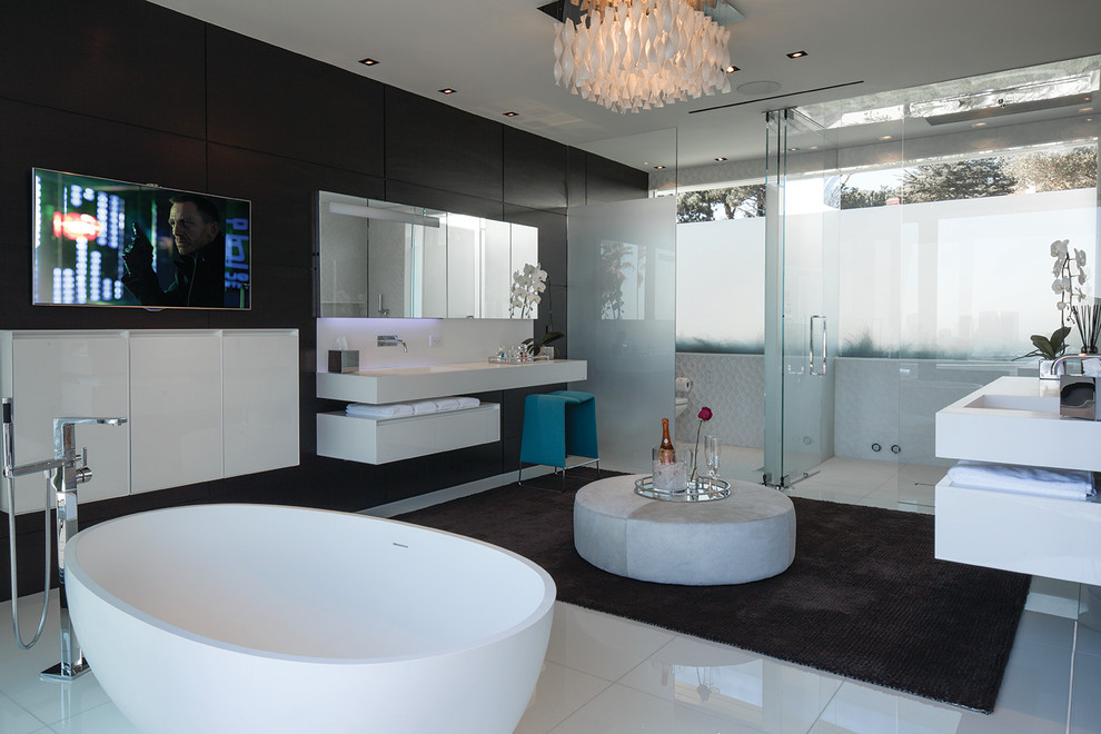Modern inredning av ett badrum, med ett avlångt handfat, släta luckor, vita skåp, ett fristående badkar, en kantlös dusch, vit kakel och svarta väggar