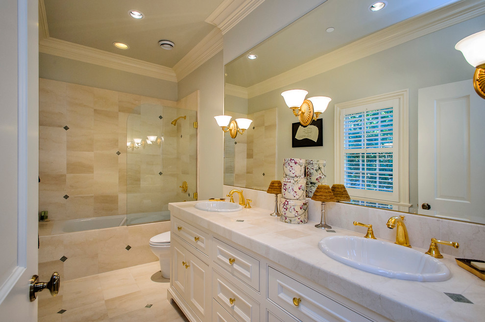 Modelo de cuarto de baño clásico con lavabo encastrado, puertas de armario blancas, bañera empotrada, combinación de ducha y bañera, baldosas y/o azulejos beige y armarios con paneles empotrados