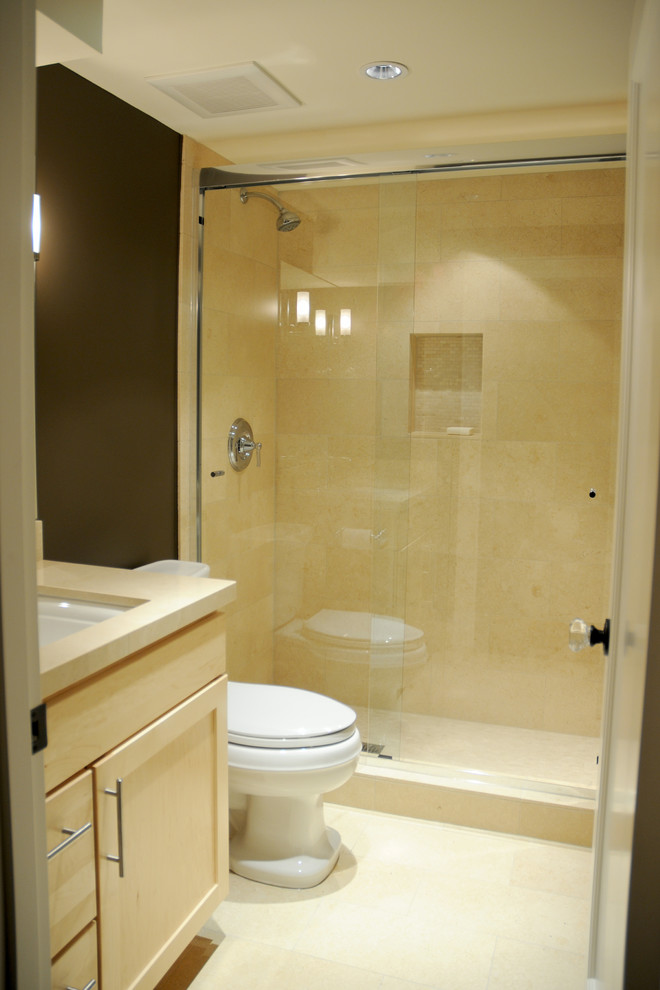 Cette image montre une salle de bain traditionnelle en bois clair avec un lavabo encastré, un placard avec porte à panneau encastré, un plan de toilette en granite, une douche d'angle, WC séparés, un carrelage beige et un carrelage de pierre.
