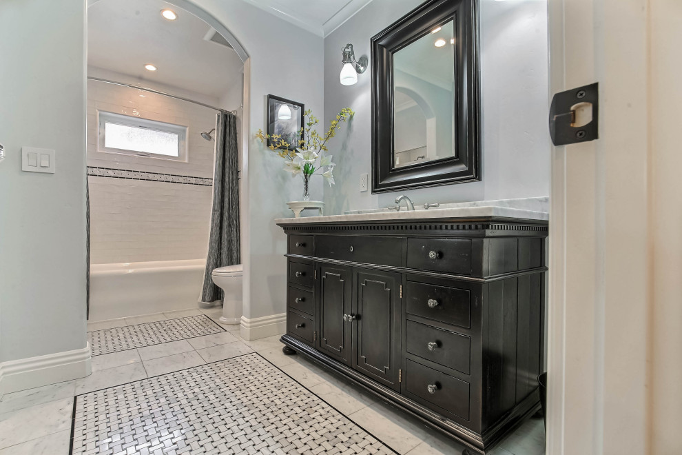 Klassisk inredning av ett vit vitt badrum, med möbel-liknande, svarta skåp, ett badkar i en alkov, en dusch/badkar-kombination, vit kakel, tunnelbanekakel, vita väggar, marmorgolv, ett undermonterad handfat, marmorbänkskiva, vitt golv och dusch med duschdraperi