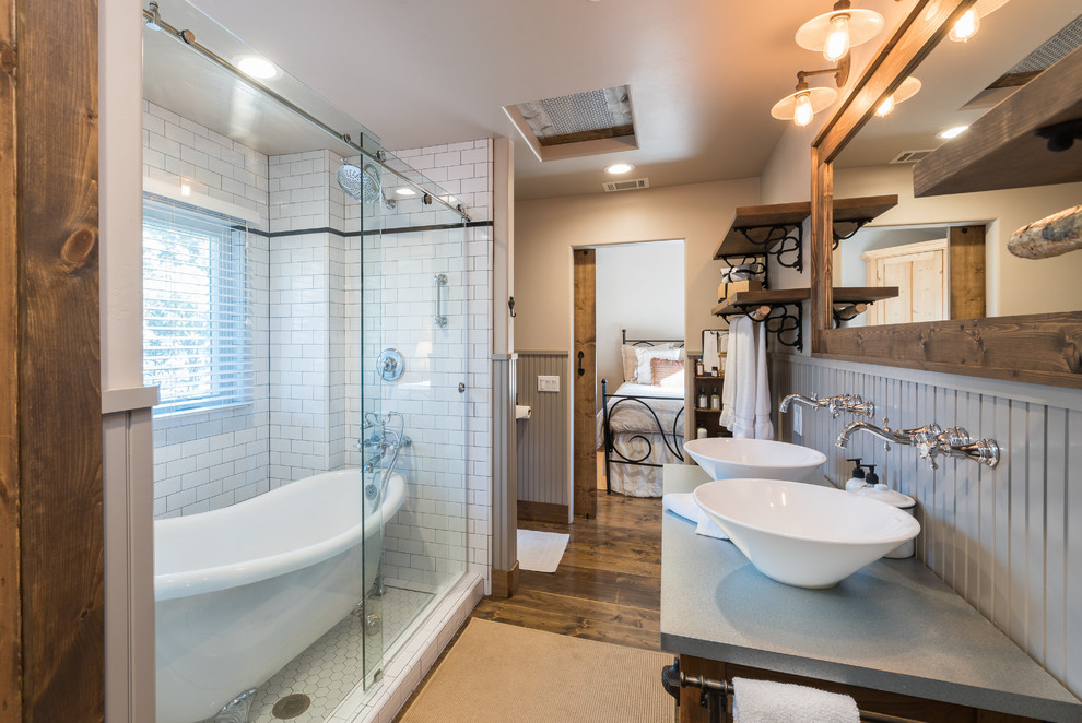 Cette image montre une salle de bain principale rustique en bois brun avec une baignoire sur pieds, un espace douche bain, un carrelage blanc, un carrelage métro, un mur beige, un sol en bois brun, une vasque, un sol marron, une cabine de douche à porte coulissante et un plan de toilette gris.