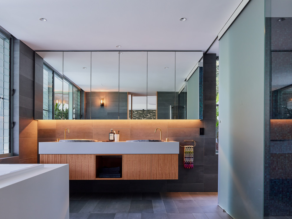 На фото: ванная комната среднего размера в современном стиле с плоскими фасадами, фасадами цвета дерева среднего тона, серой плиткой, серыми стенами, накладной раковиной, серым полом и серой столешницей