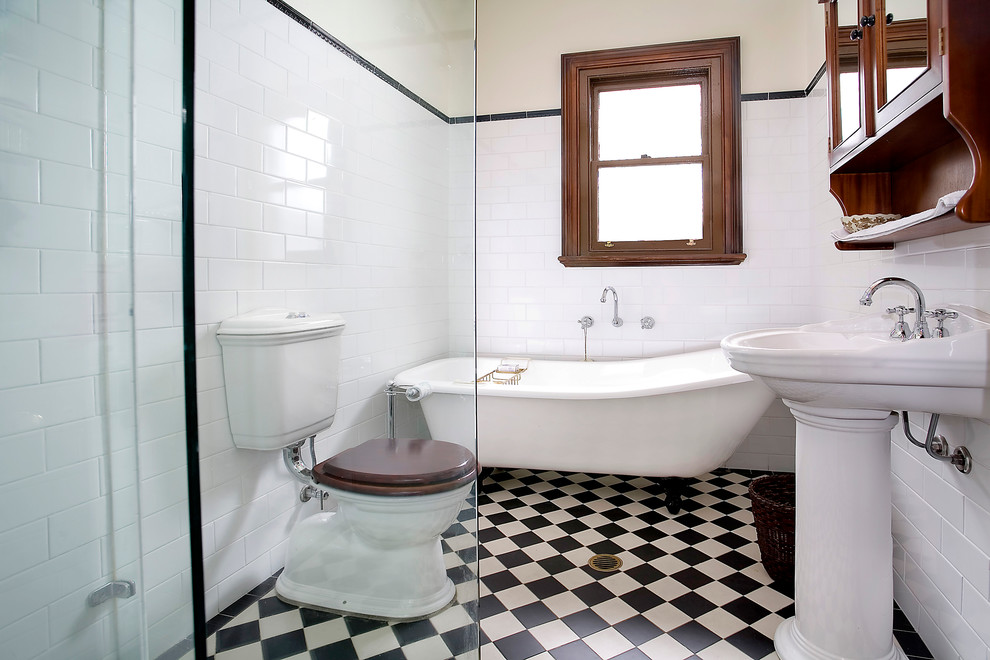 На фото: ванная комната в классическом стиле с отдельно стоящей ванной, раковиной с пьедесталом, черно-белой плиткой и разноцветным полом