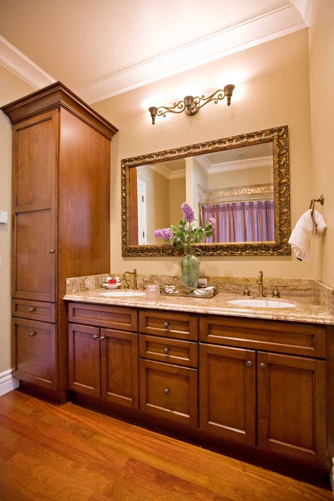 Klassisk inredning av ett mellanstort beige beige badrum, med granitbänkskiva, ett undermonterad handfat, skåp i shakerstil, skåp i mellenmörkt trä, en dusch/badkar-kombination, beige kakel, porslinskakel, beige väggar, mellanmörkt trägolv, ett badkar i en alkov, en toalettstol med hel cisternkåpa, brunt golv och dusch med duschdraperi