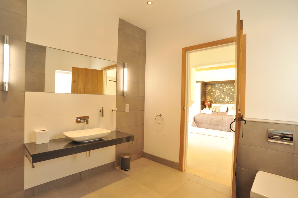 Inredning av ett modernt en-suite badrum, med ett konsol handfat, släta luckor, grå skåp, ett fristående badkar, en öppen dusch, en vägghängd toalettstol, grå kakel, porslinskakel, vita väggar och klinkergolv i porslin