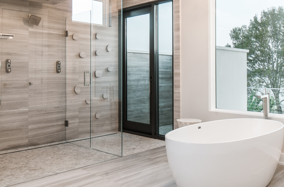 Inspiration for a large modern ensuite bathroom in Toronto with flat-panel cabinets, medium wood cabinets, a freestanding bath, a corner shower, beige walls, porcelain flooring, a submerged sink, grey floors and a hinged door.