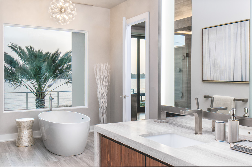 Photo of a large modern ensuite bathroom in Toronto with flat-panel cabinets, medium wood cabinets, a freestanding bath, beige walls, a submerged sink, porcelain flooring, grey floors, a corner shower and a hinged door.