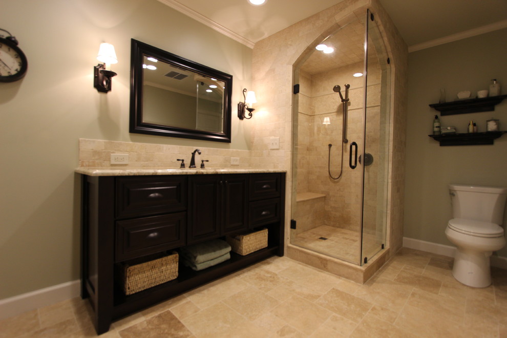 Klassisk inredning av ett litet en-suite badrum, med ett undermonterad handfat, möbel-liknande, skåp i mörkt trä, granitbänkskiva, en dusch i en alkov, en toalettstol med separat cisternkåpa, brun kakel, stenkakel, gröna väggar och travertin golv