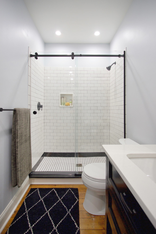 Inredning av ett klassiskt litet vit vitt badrum med dusch, med luckor med infälld panel, svarta skåp, en dusch i en alkov, vit kakel, keramikplattor, blå väggar, mellanmörkt trägolv, ett undermonterad handfat, bänkskiva i kvarts och dusch med skjutdörr