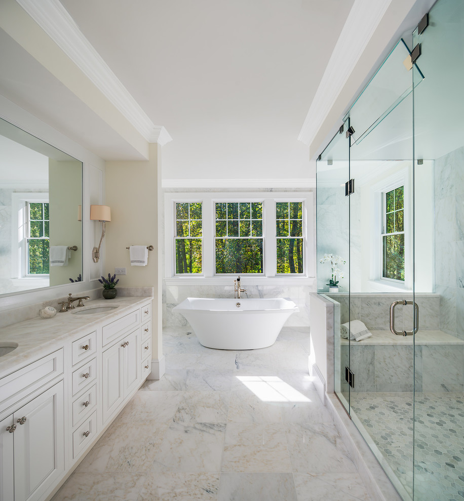 Inredning av ett klassiskt stort en-suite badrum, med luckor med profilerade fronter, vita skåp, ett fristående badkar, vit kakel, marmorkakel, marmorgolv, ett undermonterad handfat, marmorbänkskiva, vitt golv, dusch med gångjärnsdörr och beige väggar