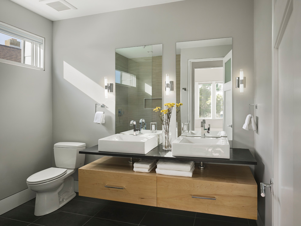 Example of a small trendy master gray tile porcelain tile and black floor bathroom design in Other with flat-panel cabinets, light wood cabinets, a two-piece toilet, gray walls, a console sink and quartzite countertops