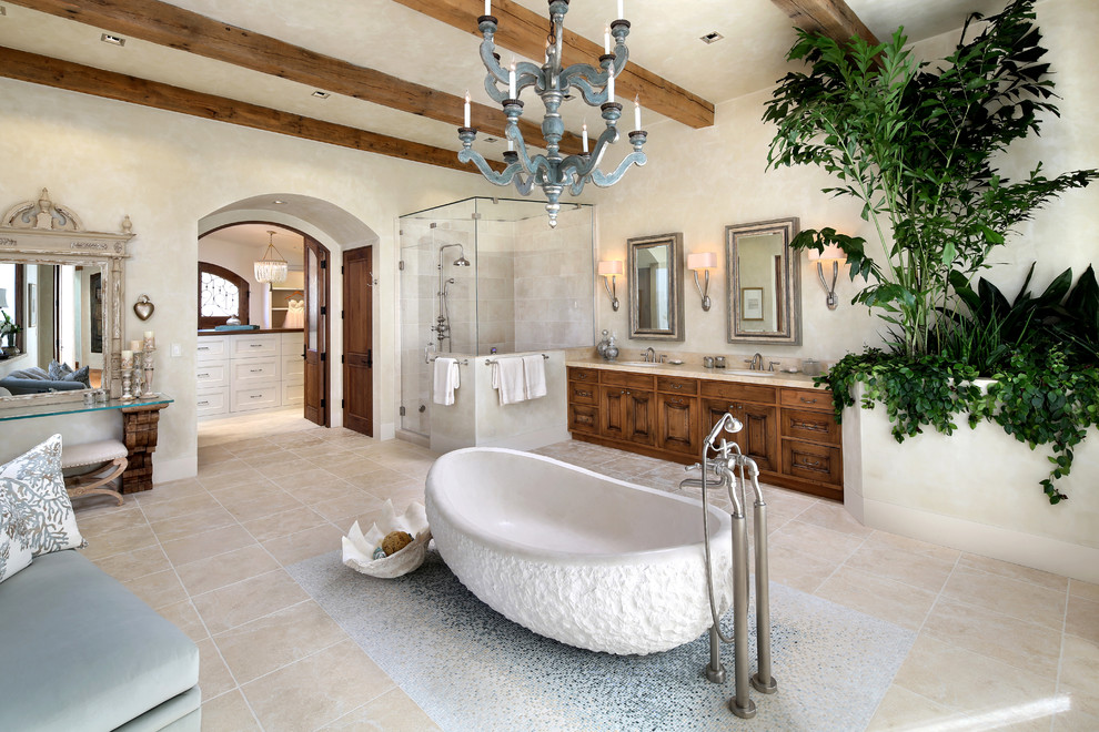 Cette image montre une très grande salle de bain principale méditerranéenne en bois brun avec un carrelage beige, une baignoire indépendante, un lavabo encastré, un mur beige, un sol en travertin, une cabine de douche à porte battante, un placard avec porte à panneau encastré, une douche d'angle, des carreaux de céramique et un sol beige.