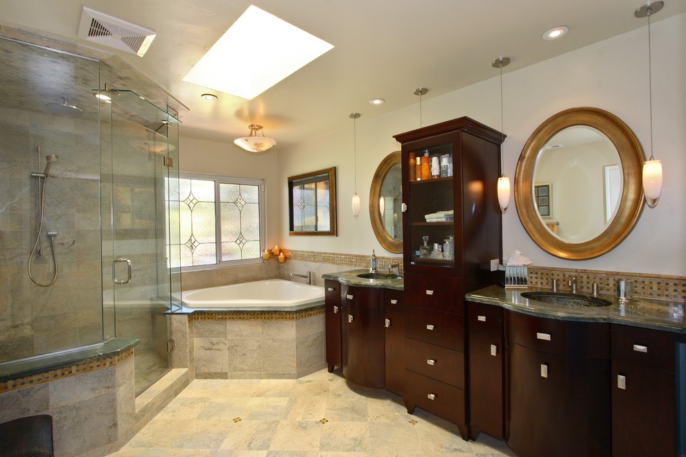 Cette image montre une salle de bain design en bois foncé avec un placard à porte plane, une baignoire d'angle, une douche d'angle, un carrelage beige, un lavabo posé, un plan de toilette en marbre, un carrelage de pierre, un mur beige et un sol en marbre.