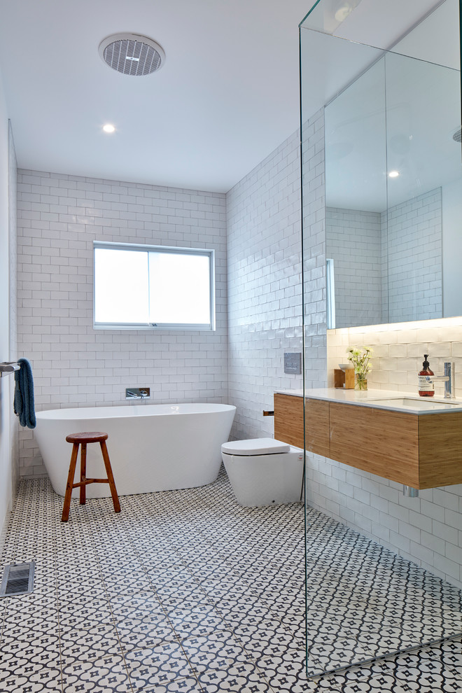 Medium sized contemporary family bathroom in Melbourne with an open shower, light wood cabinets, a freestanding bath, a corner shower, a one-piece toilet, white tiles, metro tiles, white walls, cement flooring, a submerged sink, marble worktops, multi-coloured floors, white worktops and flat-panel cabinets.