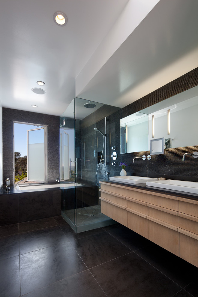 Источник вдохновения для домашнего уюта: большая главная ванная комната с настольной раковиной, плоскими фасадами, светлыми деревянными фасадами, столешницей из оникса, полновстраиваемой ванной, угловым душем и черной плиткой