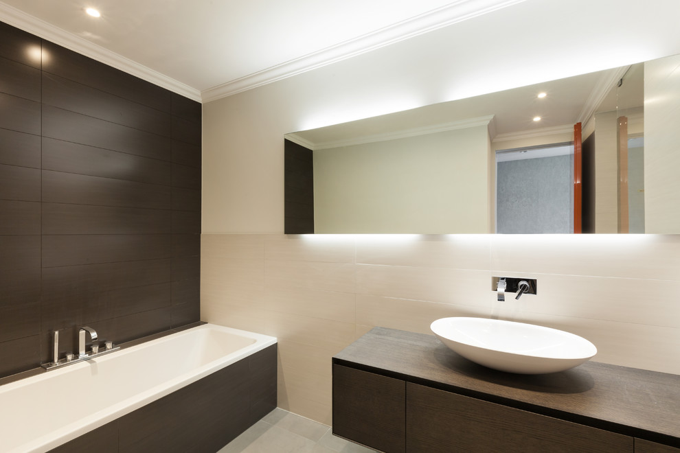 Photo of a medium sized modern ensuite bathroom in Other with flat-panel cabinets, brown cabinets, a built-in bath, black tiles, brown tiles, white tiles, stone tiles, multi-coloured walls, porcelain flooring, a vessel sink, wooden worktops and grey floors.