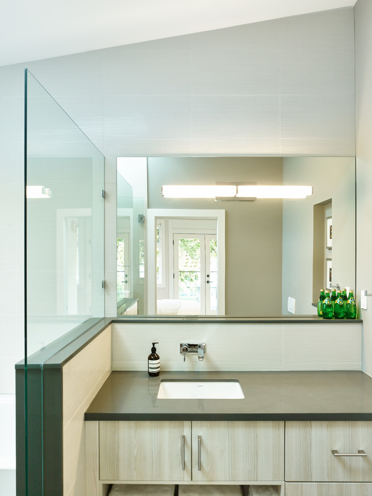 Exemple d'une salle de bain tendance en bois clair avec un lavabo encastré, un placard à porte plane, un plan de toilette en granite, WC suspendus, un carrelage blanc, des carreaux de céramique, un mur gris et un sol en carrelage de céramique.