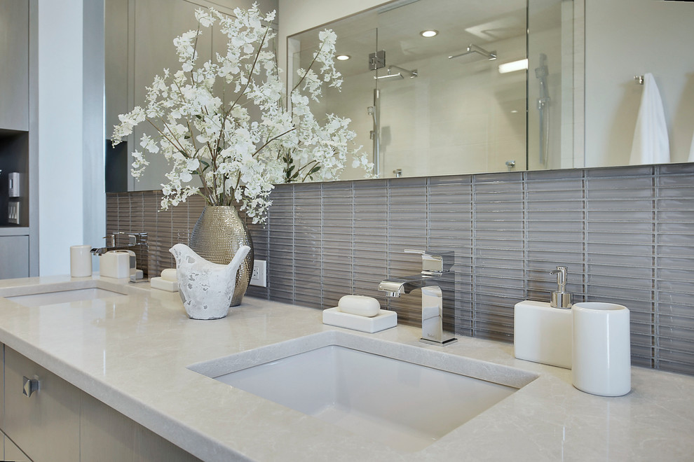Пример оригинального дизайна: главная ванная комната среднего размера в современном стиле с плоскими фасадами, серыми фасадами, угловым душем, унитазом-моноблоком, серой плиткой, стеклянной плиткой, серыми стенами, полом из керамогранита, врезной раковиной, столешницей из искусственного кварца, белым полом и душем с распашными дверями