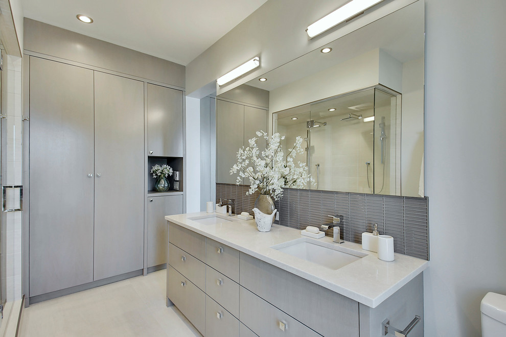 На фото: главная ванная комната среднего размера в современном стиле с плоскими фасадами, серыми фасадами, угловым душем, унитазом-моноблоком, серой плиткой, стеклянной плиткой, серыми стенами, полом из керамогранита, врезной раковиной, столешницей из искусственного кварца, белым полом и душем с распашными дверями