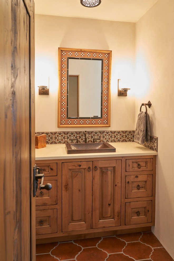 Cette photo montre une salle de bain sud-ouest américain en bois brun avec un placard avec porte à panneau surélevé, un carrelage multicolore, un mur beige, tomettes au sol, un lavabo posé, un sol rouge, un plan de toilette blanc, meuble simple vasque et meuble-lavabo encastré.