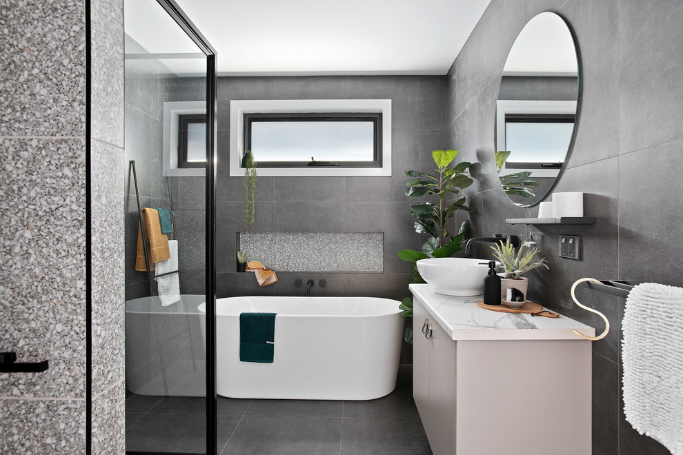 Photo of a small contemporary ensuite bathroom in Other with a freestanding bath, a corner shower, grey tiles, ceramic tiles, ceramic flooring, grey floors, a hinged door, flat-panel cabinets, grey cabinets, a vessel sink, laminate worktops and white worktops.