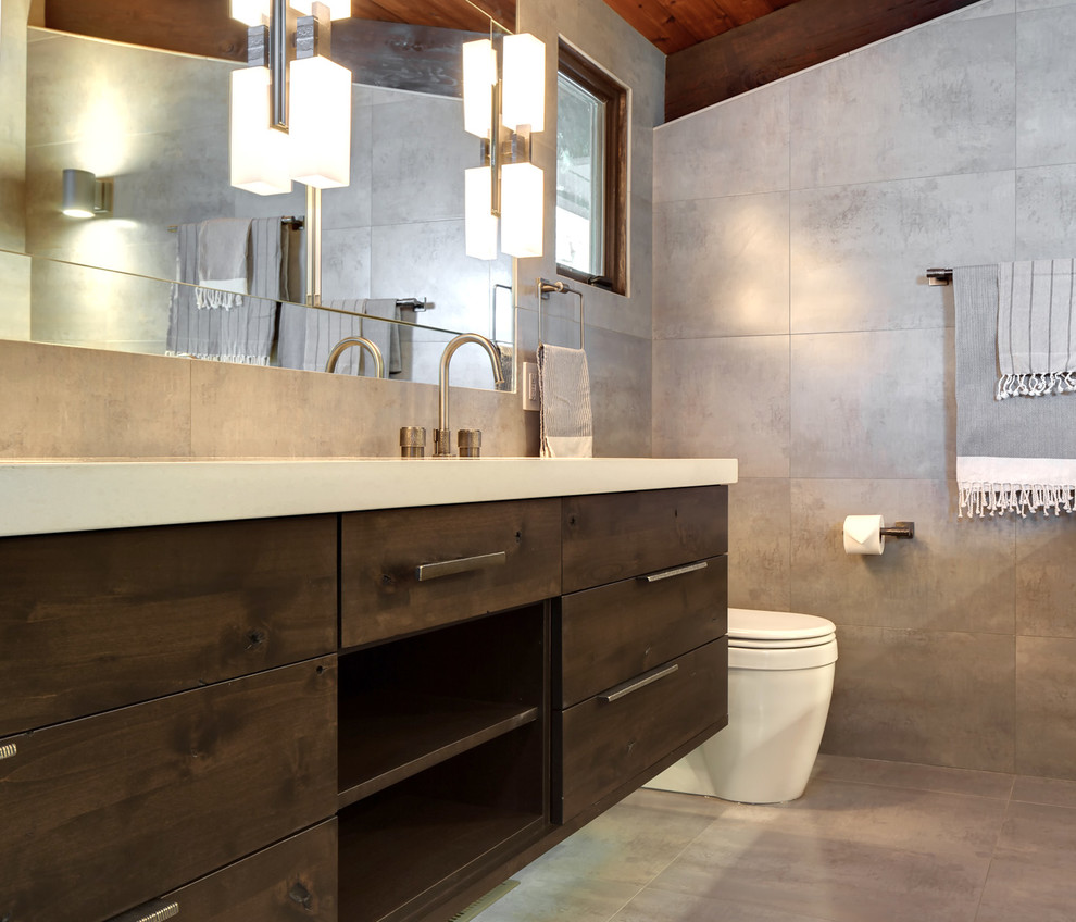 Стильный дизайн: главная ванная комната в современном стиле с врезной раковиной, плоскими фасадами, темными деревянными фасадами, столешницей из искусственного кварца, унитазом-моноблоком и серой плиткой - последний тренд
