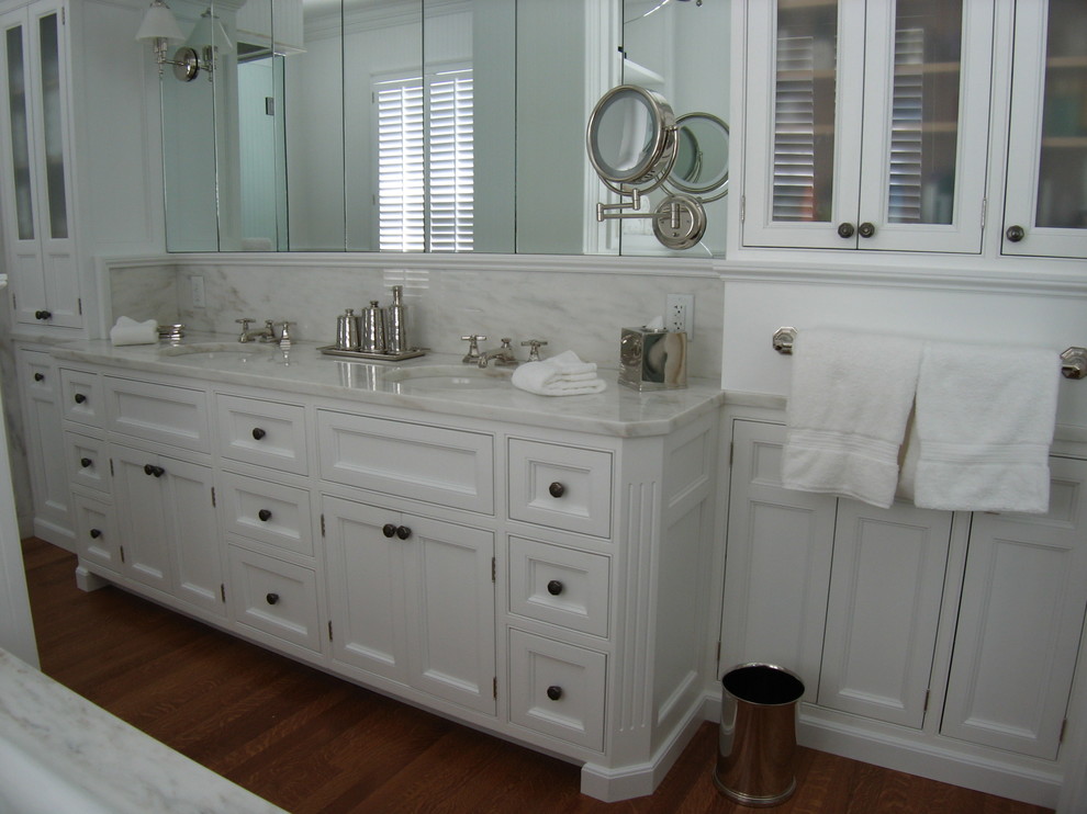 Inredning av ett klassiskt stort en-suite badrum, med ett undermonterad handfat, en toalettstol med separat cisternkåpa, vita väggar, mellanmörkt trägolv, luckor med profilerade fronter, vita skåp, marmorbänkskiva och en dusch i en alkov