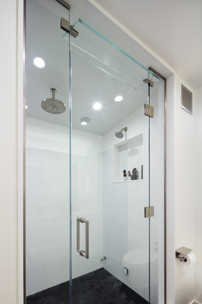 This is an example of a large contemporary ensuite wet room bathroom in New York with flat-panel cabinets, white cabinets, a wall mounted toilet, white tiles, porcelain tiles, white walls, porcelain flooring, a submerged sink, engineered stone worktops, black floors and a hinged door.