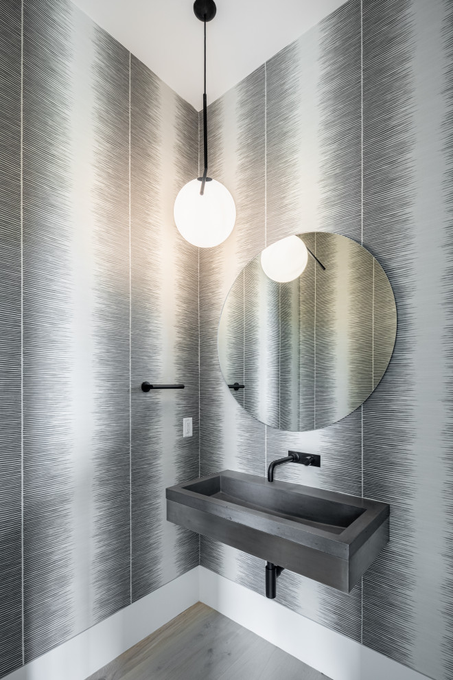 Inredning av ett modernt mellanstort grå grått badrum med dusch, med öppna hyllor, grå skåp, en toalettstol med separat cisternkåpa, ljust trägolv, ett väggmonterat handfat, bänkskiva i betong och brunt golv