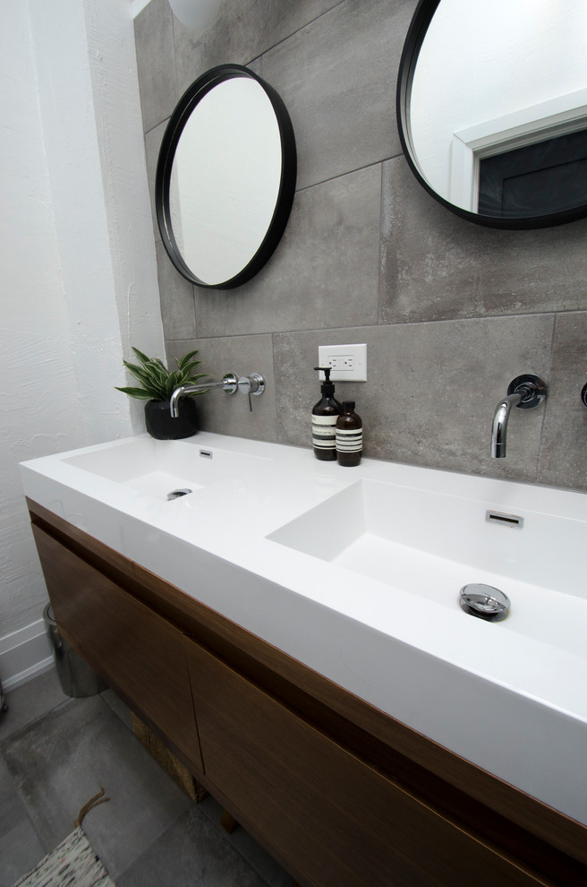 Modern inredning av ett mellanstort vit vitt badrum med dusch, med släta luckor, skåp i mellenmörkt trä, en hörndusch, en toalettstol med separat cisternkåpa, grå kakel, porslinskakel, vita väggar, klinkergolv i porslin, ett integrerad handfat, bänkskiva i akrylsten, grått golv och med dusch som är öppen