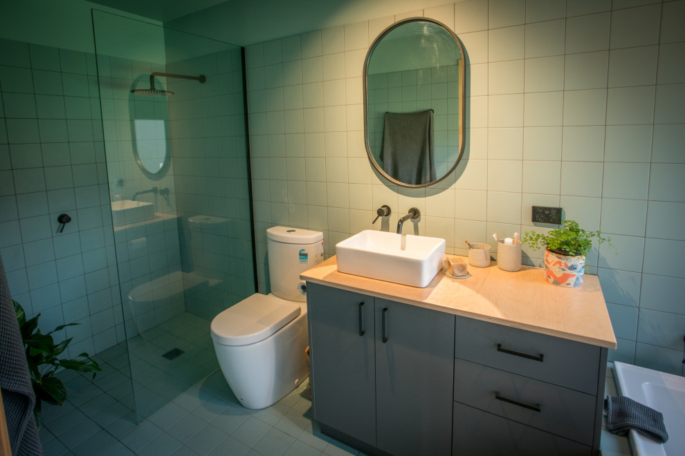 На фото: маленькая главная ванная комната в современном стиле с фасадами островного типа, серыми фасадами, угловой ванной, открытым душем, унитазом-моноблоком, зеленой плиткой, керамической плиткой, зелеными стенами, полом из цементной плитки, настольной раковиной, столешницей из дерева, зеленым полом, открытым душем, бежевой столешницей, тумбой под одну раковину и подвесной тумбой для на участке и в саду с
