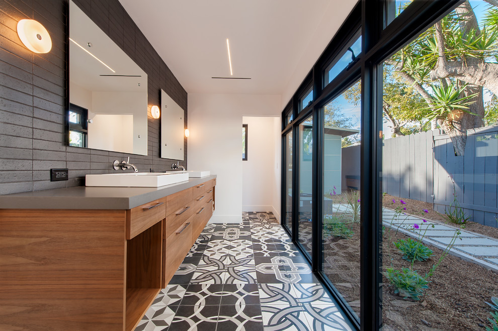 Large modern ensuite bathroom in San Diego with flat-panel cabinets, medium wood cabinets, an alcove shower, a wall mounted toilet, black and white tiles, cement tiles, white walls, concrete flooring, a trough sink, engineered stone worktops and multi-coloured floors.