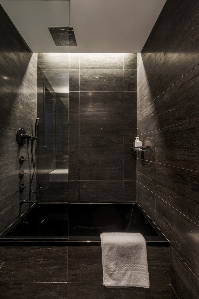 Inspiration for a small modern ensuite bathroom in New York with flat-panel cabinets, black cabinets, a built-in bath, a shower/bath combination, a two-piece toilet, black tiles, stone slabs, black walls, an integrated sink and solid surface worktops.