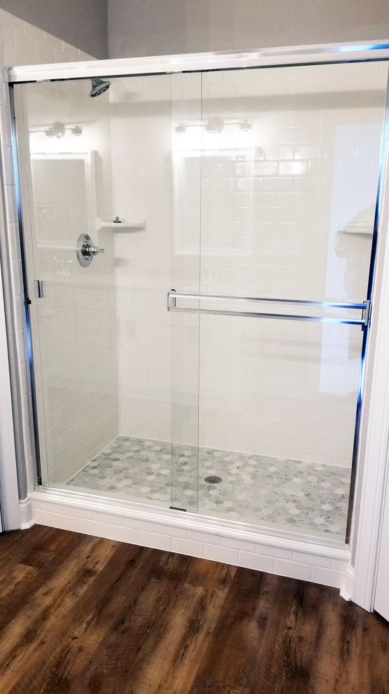 Foto de cuarto de baño de estilo americano de tamaño medio con ducha empotrada, baldosas y/o azulejos blancos, paredes beige, suelo laminado, suelo marrón y ducha con puerta corredera