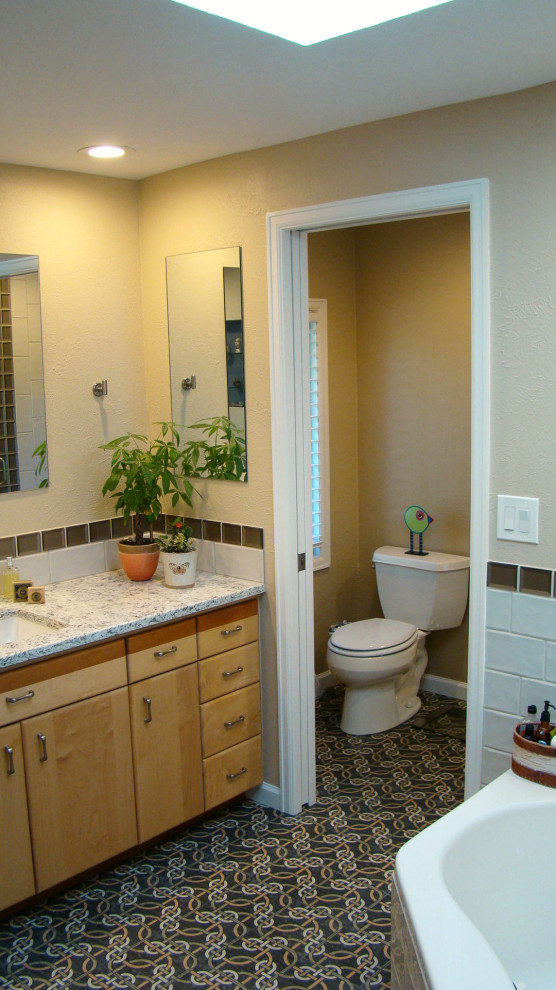 Photo of a medium sized traditional ensuite bathroom in Denver with flat-panel cabinets, medium wood cabinets, a corner bath, an alcove shower, a two-piece toilet, grey tiles, porcelain tiles, grey walls, porcelain flooring, a submerged sink, engineered stone worktops, multi-coloured floors, a hinged door, multi-coloured worktops, a single sink and a built in vanity unit.