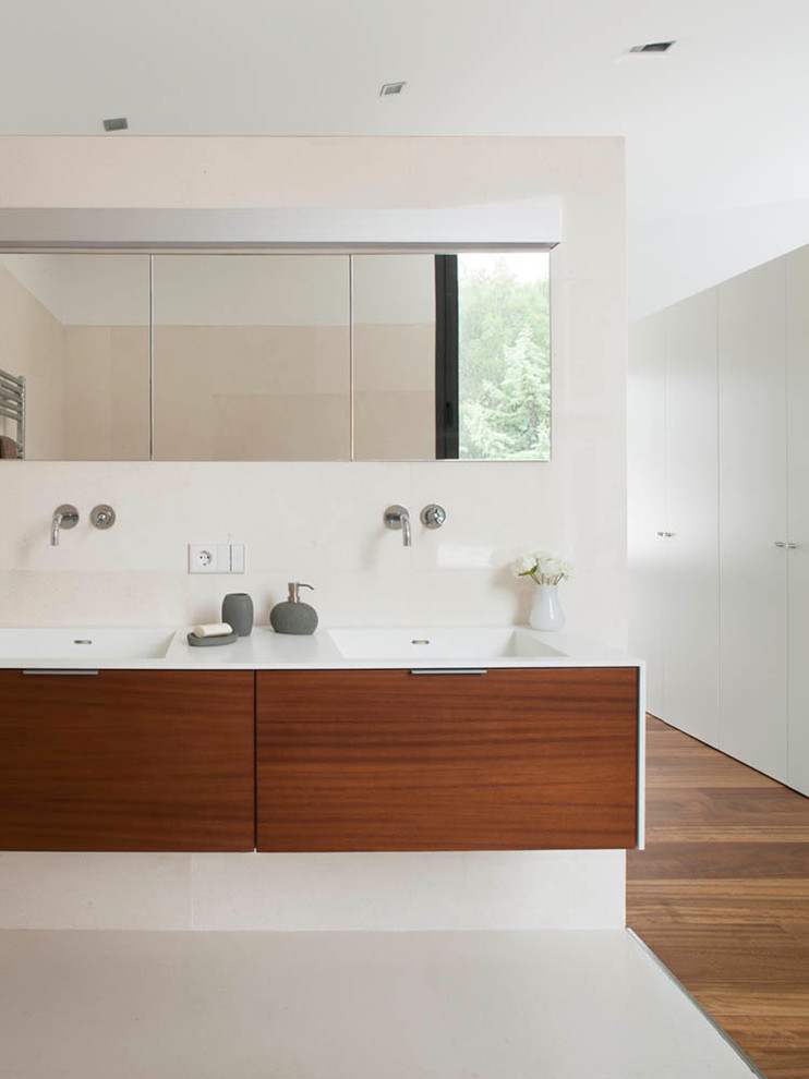 Cette image montre une salle de bain principale minimaliste en bois brun avec un placard à porte plane, un plan de toilette en surface solide, un carrelage beige, un carrelage de pierre et un sol en calcaire.