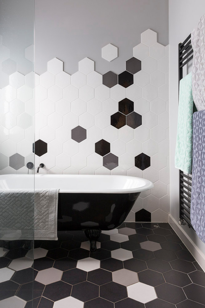 Aménagement d'une salle de bain contemporaine avec une baignoire sur pieds, un carrelage noir et blanc, un mur gris et un sol multicolore.
