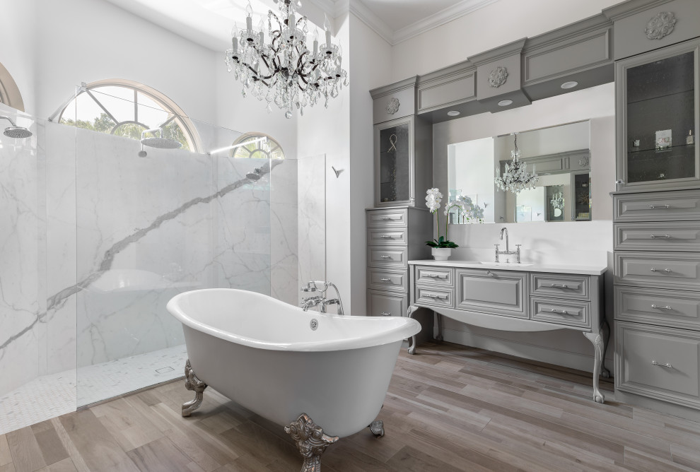 Bild på ett medelhavsstil vit vitt badrum, med luckor med upphöjd panel, grå skåp, ett badkar med tassar, vit kakel, stenhäll, vita väggar, mellanmörkt trägolv, ett undermonterad handfat och brunt golv