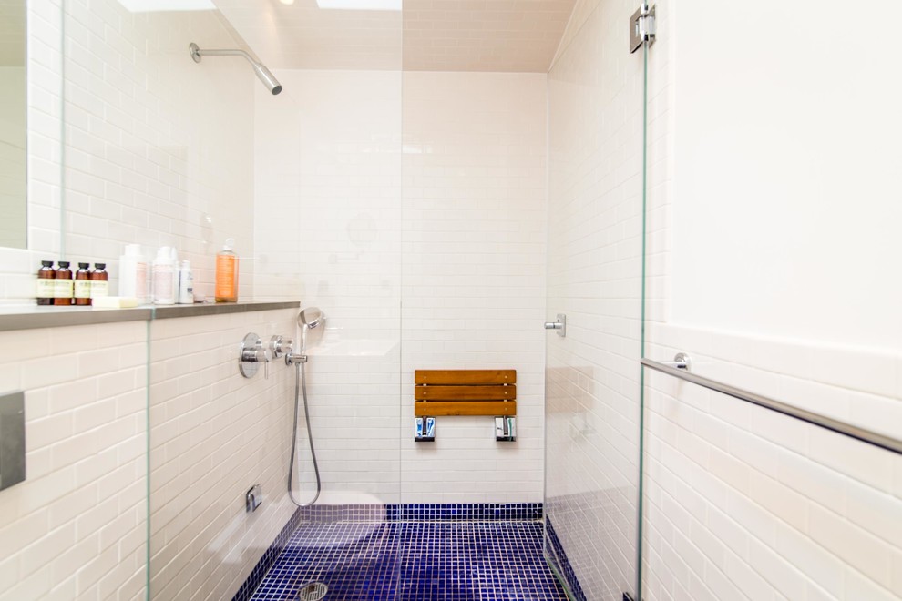 Imagen de sauna costera de tamaño medio con paredes blancas, suelo de madera clara, lavabo suspendido, bañera empotrada, sanitario de pared, baldosas y/o azulejos azules y baldosas y/o azulejos de porcelana