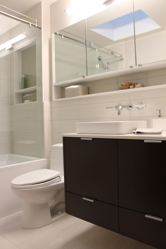 Bild på ett mellanstort funkis en-suite badrum, med ett fristående handfat, släta luckor, skåp i mörkt trä, bänkskiva i kvarts, ett badkar i en alkov, en toalettstol med hel cisternkåpa, grå kakel, porslinskakel, grå väggar, klinkergolv i porslin och en dusch/badkar-kombination