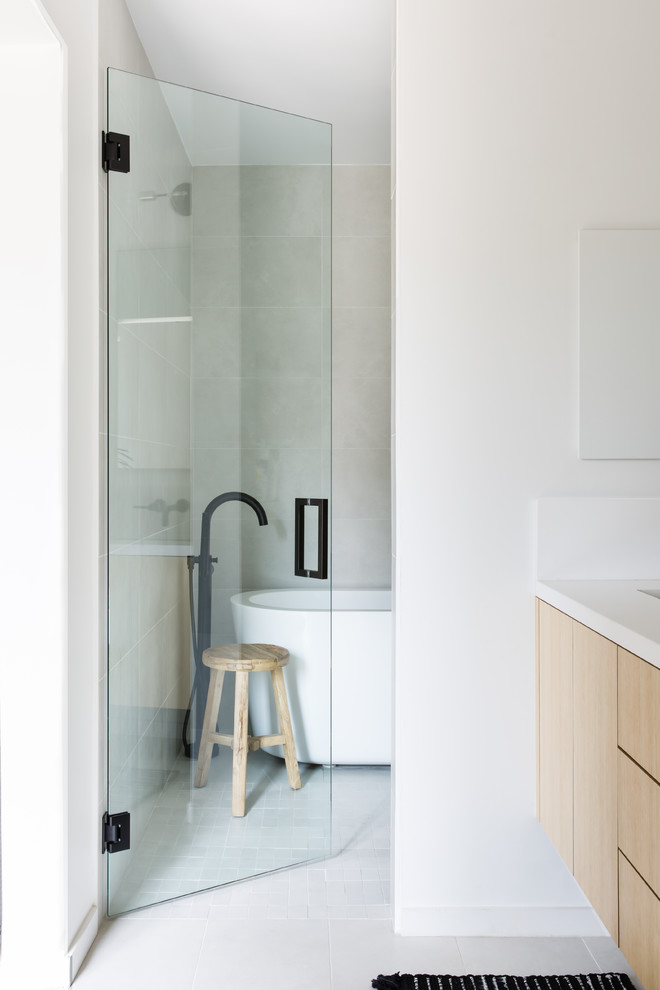 Photo of a medium sized scandi ensuite wet room bathroom in Los Angeles with flat-panel cabinets, light wood cabinets, a freestanding bath, a two-piece toilet, white tiles, ceramic tiles, white walls, ceramic flooring, a submerged sink, engineered stone worktops, white floors and a hinged door.
