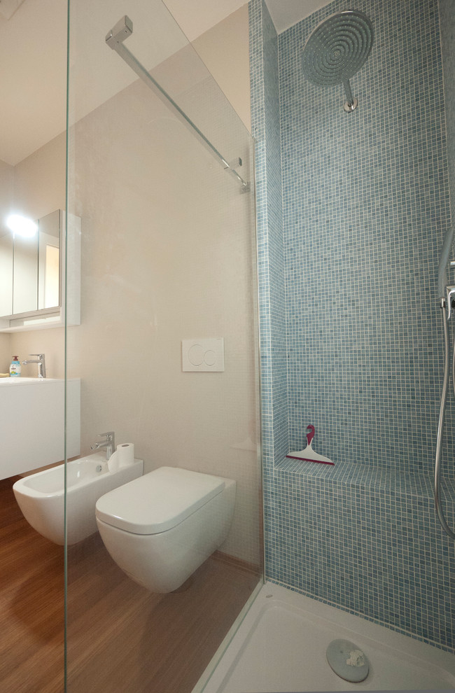 This is an example of a medium sized modern ensuite bathroom in Milan with an integrated sink, flat-panel cabinets, white cabinets, engineered stone worktops, a walk-in shower, a wall mounted toilet, blue tiles, glass tiles, beige walls and bamboo flooring.