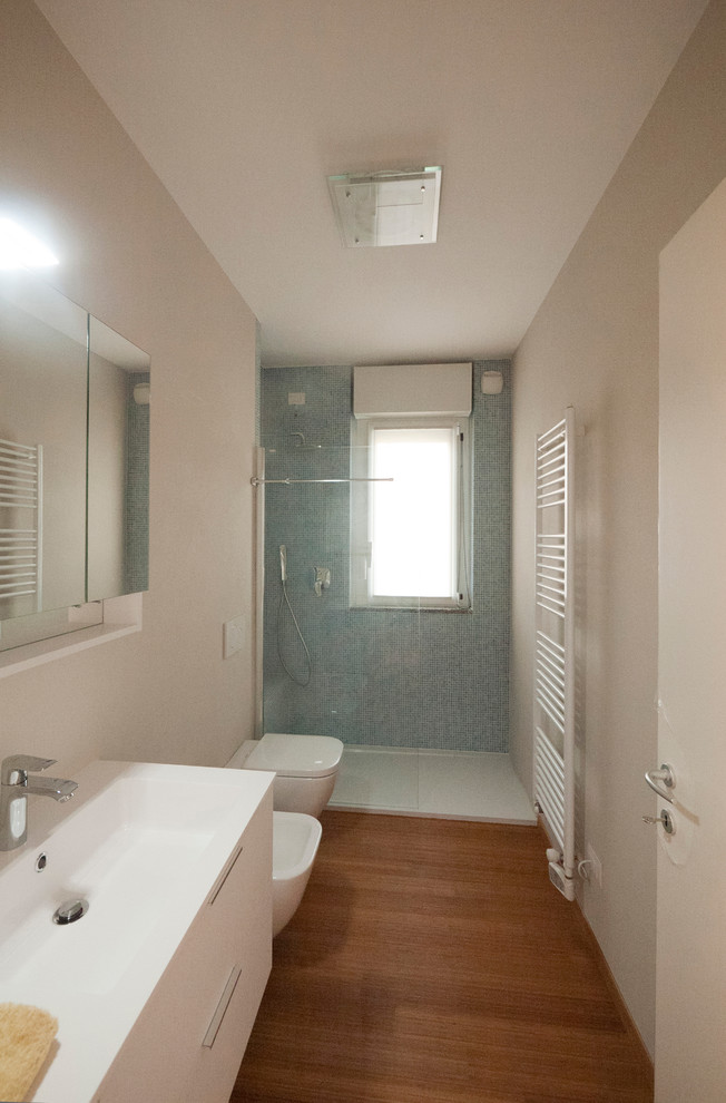 На фото: главная ванная комната среднего размера в стиле модернизм с монолитной раковиной, плоскими фасадами, белыми фасадами, столешницей из искусственного кварца, открытым душем, инсталляцией, синей плиткой, стеклянной плиткой, бежевыми стенами и полом из бамбука с