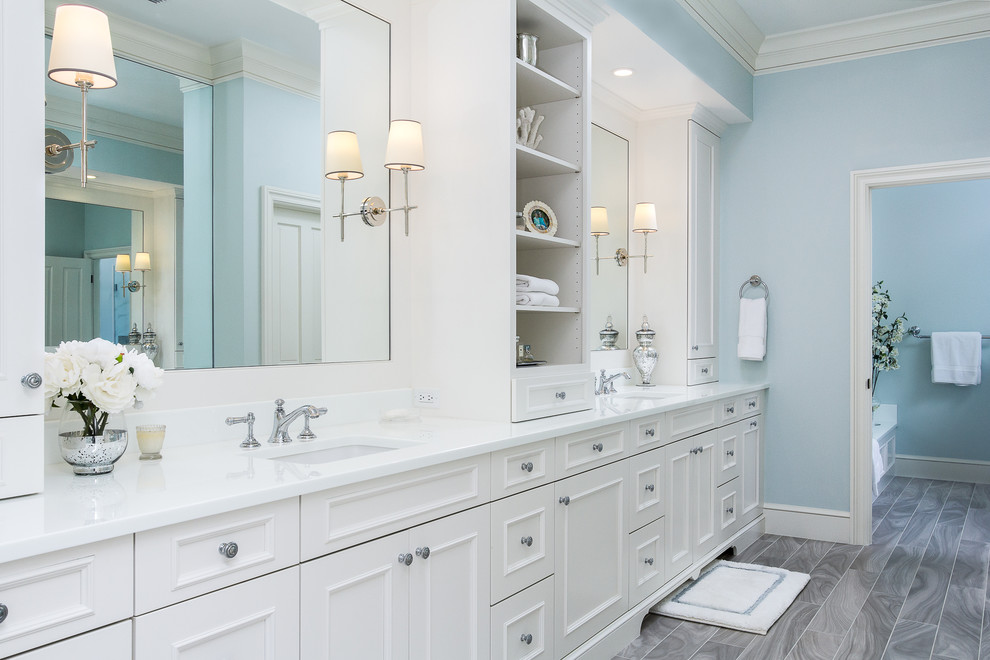 Cette photo montre une grande salle de bain principale bord de mer avec un placard en trompe-l'oeil, des portes de placard blanches, une baignoire encastrée, une douche ouverte, WC à poser, un carrelage gris, des carreaux de porcelaine, un mur bleu, un sol en carrelage de porcelaine, un lavabo encastré et un plan de toilette en verre.