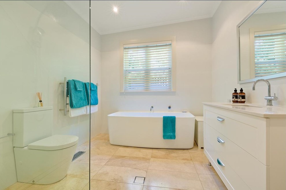 Inspiration for a medium sized contemporary family bathroom in Sydney with shaker cabinets, white cabinets, a freestanding bath, a corner shower, a two-piece toilet, white tiles, cement tiles, white walls, limestone flooring, a submerged sink and engineered stone worktops.
