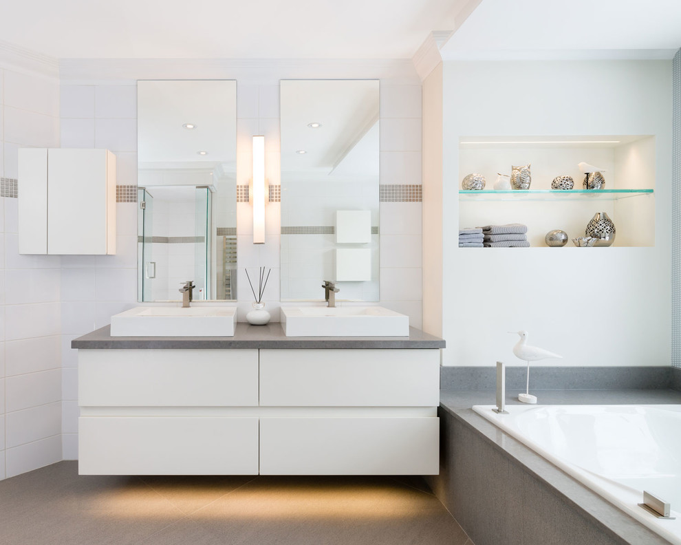 Ejemplo de cuarto de baño gris y blanco actual con lavabo sobreencimera, armarios con paneles lisos, puertas de armario blancas, bañera encastrada y baldosas y/o azulejos blancos