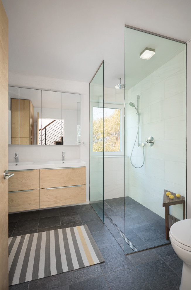 Modern inredning av ett litet en-suite badrum, med släta luckor, skåp i ljust trä, en öppen dusch, en toalettstol med hel cisternkåpa, grå kakel, stenkakel, vita väggar, skiffergolv, ett integrerad handfat och bänkskiva i kvarts